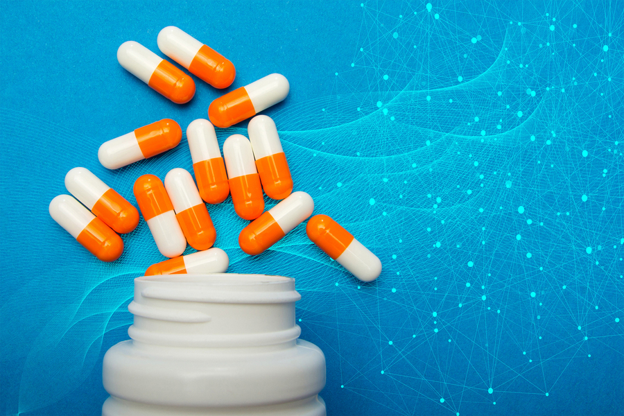 Several orange-and-white capsules spill out of a white medicine bottle onto a blue background with a digital, network-like pattern.