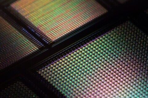 Close-up of a computer microchip or silicon wafer with a grid pattern, displaying iridescent, rainbow-like colors reflected on its surface.