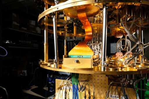 A close-up of a quantum computers intricate gold and copper components, wires, and cooling systems, set in a dimly lit lab with electronic equipment visible in the background.